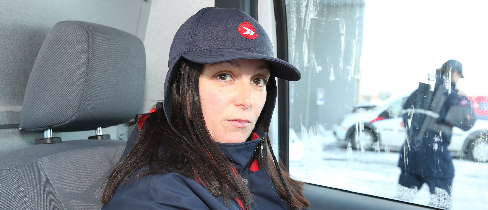 Female postal worker sitting inside of a postal truck, staring directly into the camera with a serious look on her face.